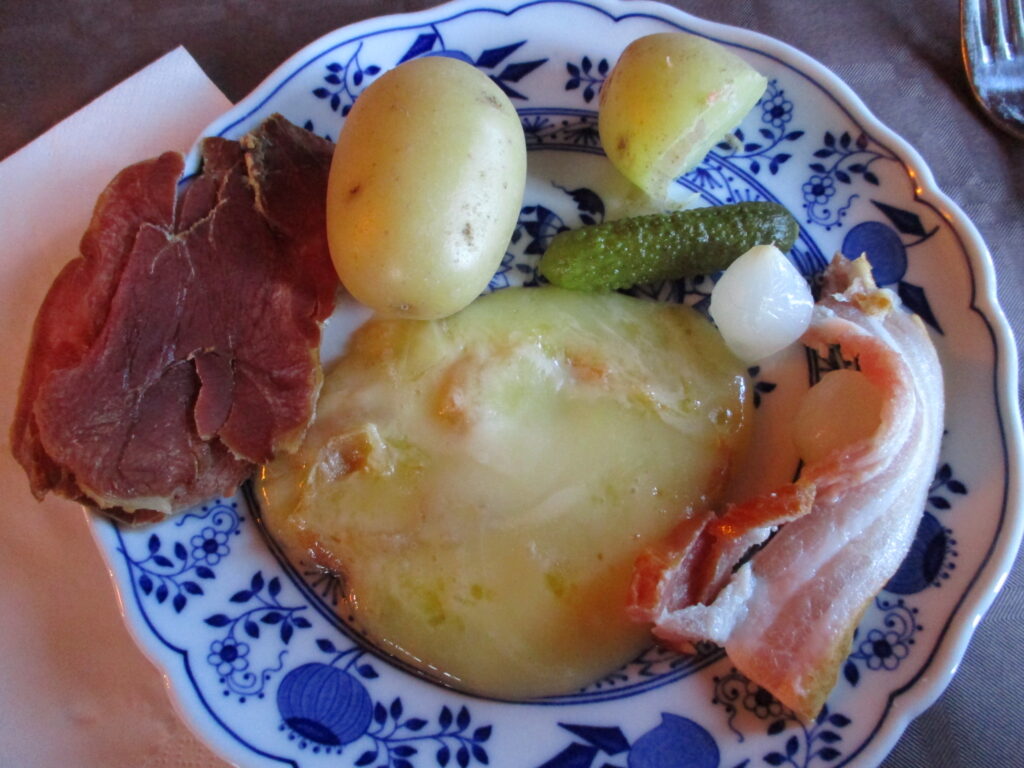 Assiette de raclette avec fromage fondu, pomme de terre, jambon , cornichon et oignon.