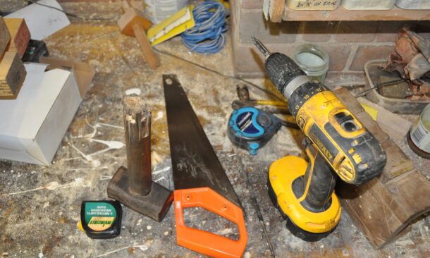 ensemble d'outils sur un établi poussièreux : mètre, marteau, scie, visseuse...