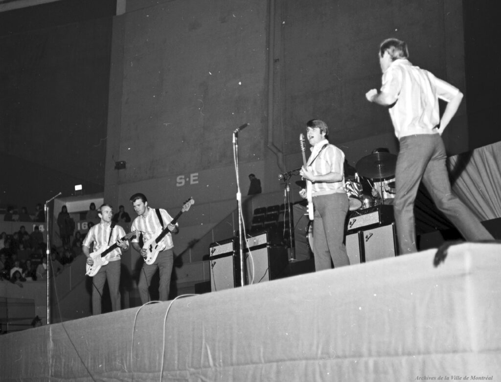 Les Beach Boys en concert à l’aréna Maurice-Richard. 19 février 1965. VM94-S32-013. Archives de la Ville de Montréal. De gauche à droite : Al Jardine, Glen Campbell (qui remplace Brian Wilson), Carl Wilson, Dennis Wilson (derrière la batterie) et Mike Love.